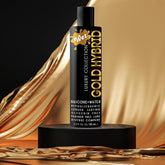 A sleek black bottle labeled "Wet Gold Hybrid Lubricant" elegantly sits on a pedestal, set against a backdrop of shimmering golden fabric. This water and silicone hybrid lubricant from Wet offers a smooth glide with its hypoallergenic, long-lasting performance formula, and is free from glycerin.